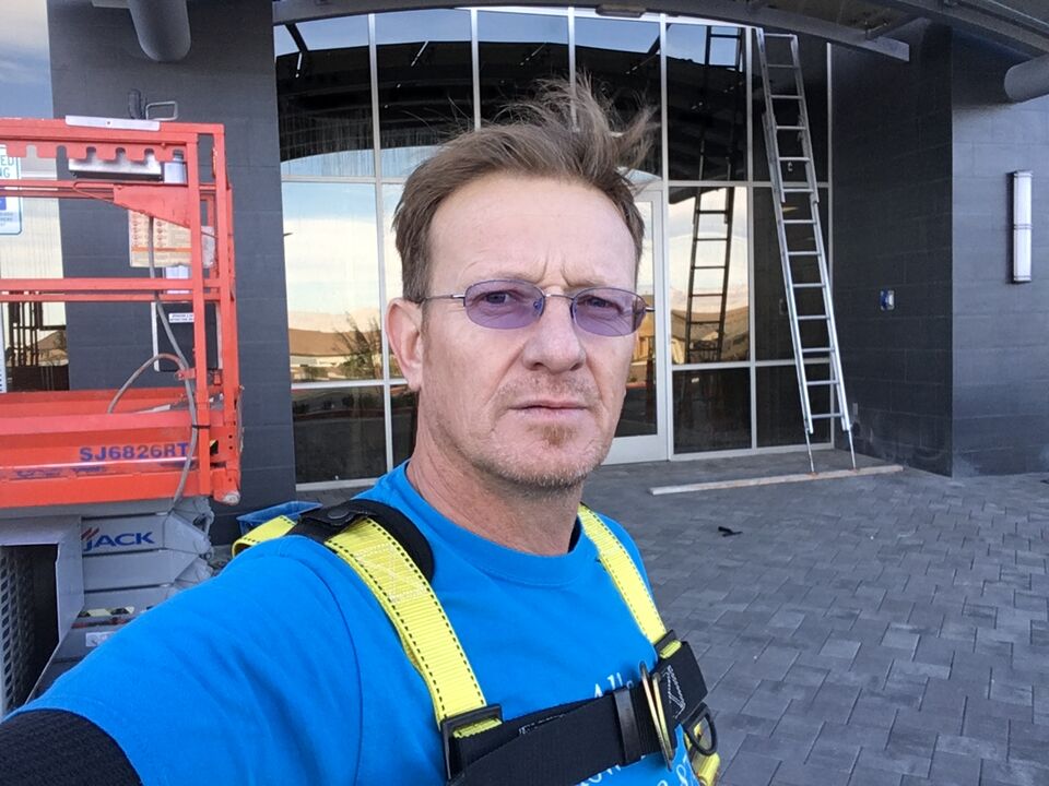 Al in a safety harness in front of a glass building with a lift and ladder behind him